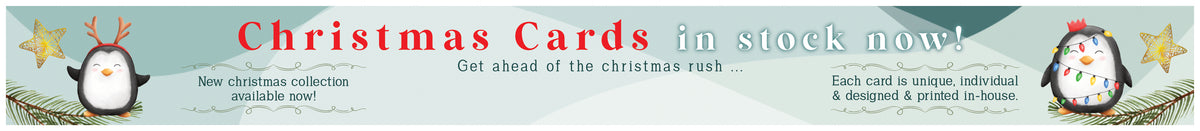 A promotional banner for Christmas cards, featuring the text 'Christmas Cards in stock now!' in red and white, with two cartoon penguins and small holiday illustrations along the bottom.